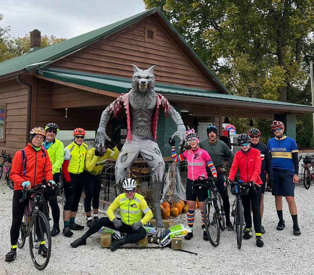 Group photo of cyclists in front of werewolf decoration in front of rural tavern.