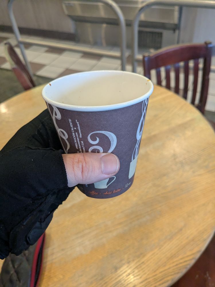 A coffee cup being held by a hand with a cycling glove on.