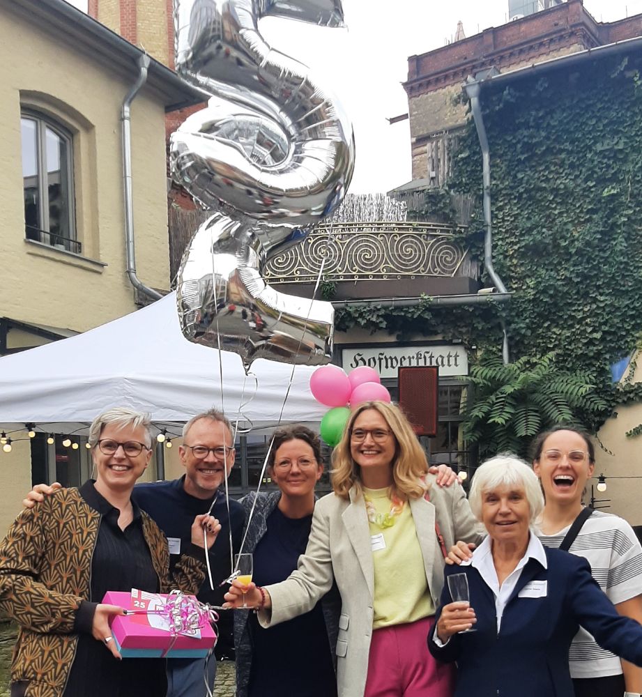 Das Team von Zukunft Fahrrad überreicht den CEOs von velo-konzept eine bunte Geschenkschachtel, an der riesige silberne Ballons mit einer 25 befestigt sind, alle lachen fröhlich in die Kamera