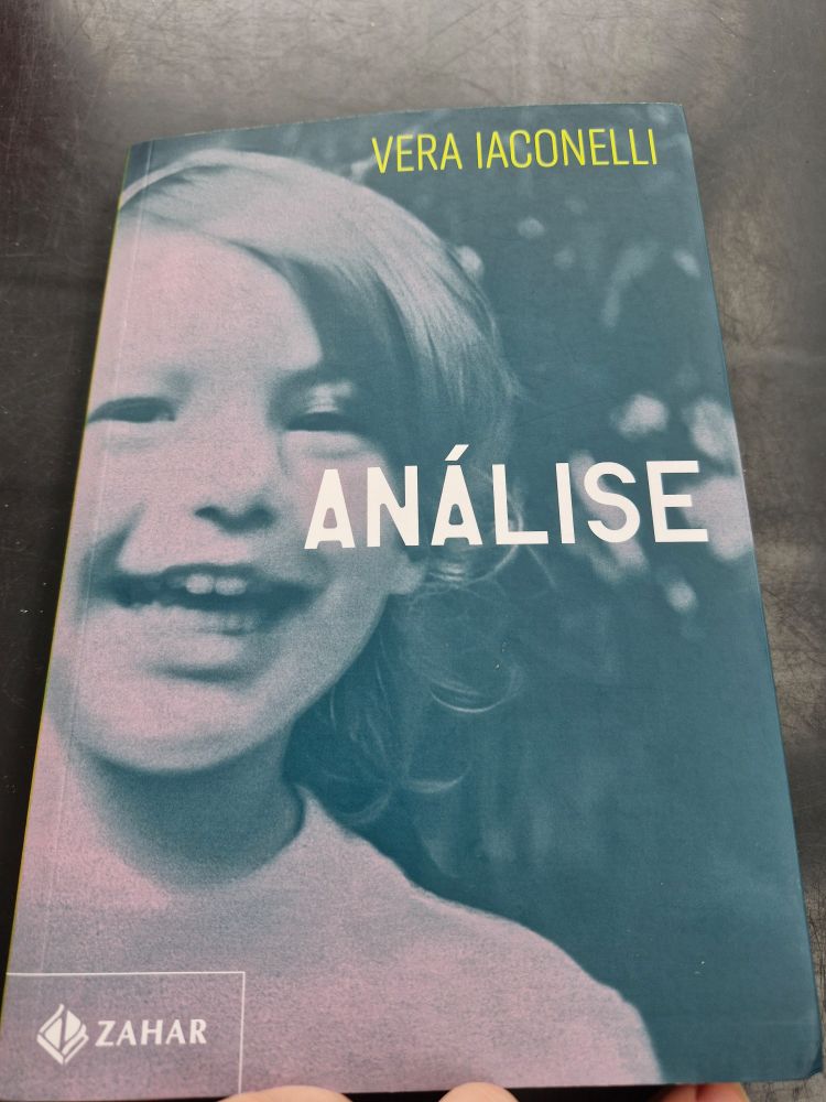 Foto da capa do livro Análise de Vera Iaconelli. A capa tem cor azulada e uma foto antiga de uma criança de 5, 6 anos com um sorrido aberto mostrando os dentes. Ela tem cabelo curto, claro e liso penteado de lado e camiseta branca.