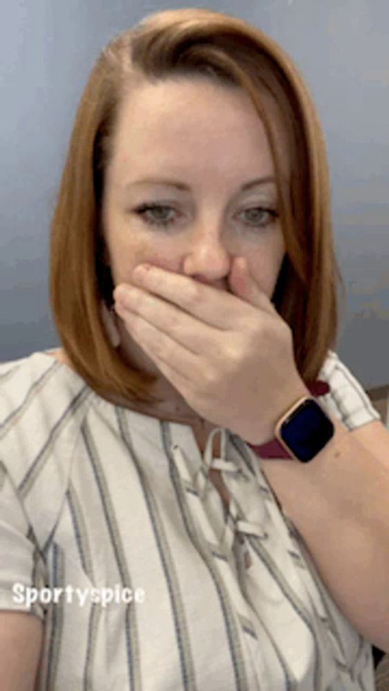 a woman in a striped shirt is covering her mouth with her hand while wearing a smart watch