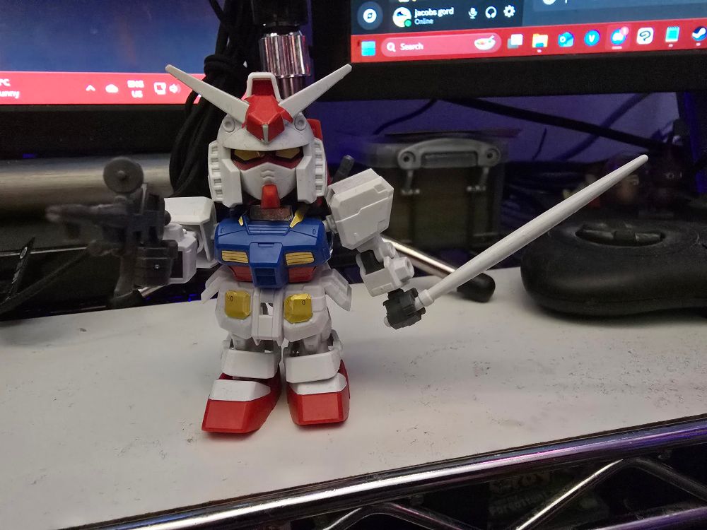SD gunpla RX-78-2 Gundam holding a white saber and pointing a gun at the camera.
