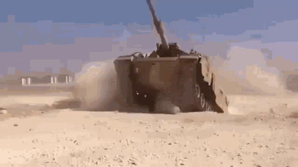 a military vehicle is driving through a desert with a blue sky in the background .