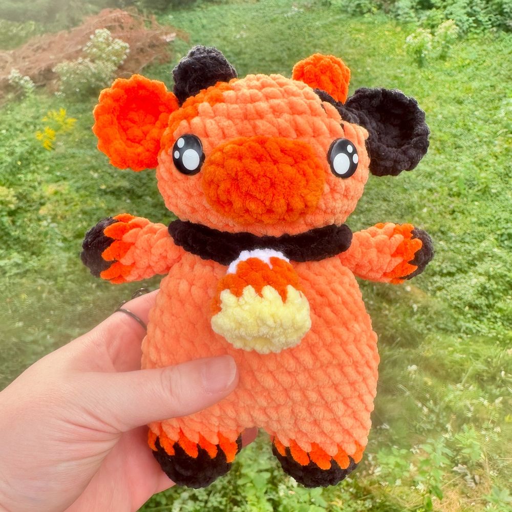 A crocheted amigurumi plushie of a cow in Halloween black and red, with a candy corn necklace.