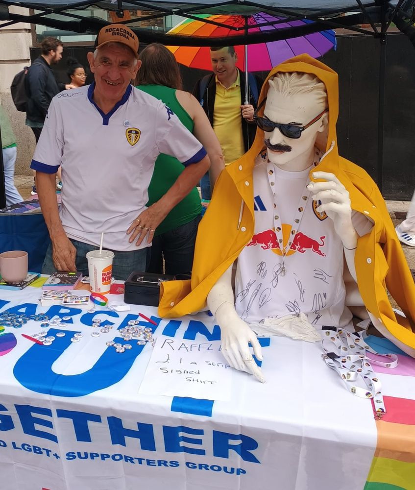 Image of mannequin in signed shirt (and raincoat), watched by Mick W at our Pride market stall