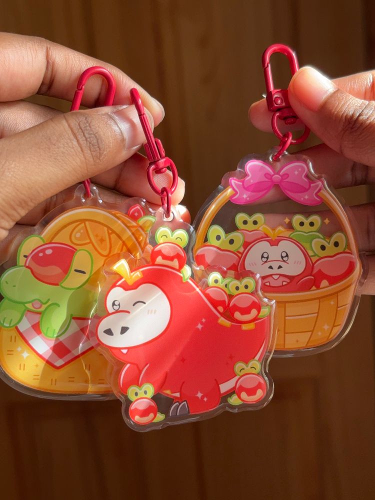 Keychains of appletun in a basket, fuecoco with applins on it, and fuecoco with applins in a basket