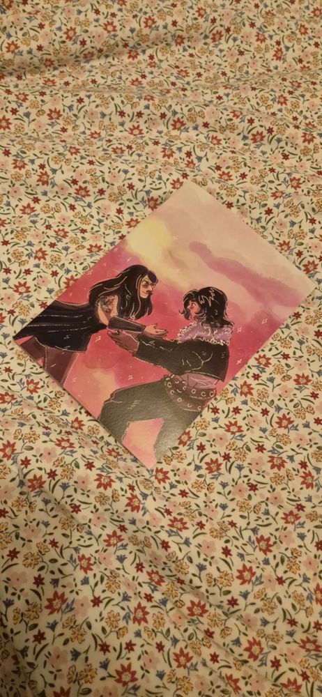 A photo featuring the cover for the proposal comic. It is lying on a bed sheet with a flower pattern. The cover is me and my partner running to each other backed by a purple and pink sky. The cover is a reference to a scene from Final Fantasy 8, and we are dressed as characters from the game to match.