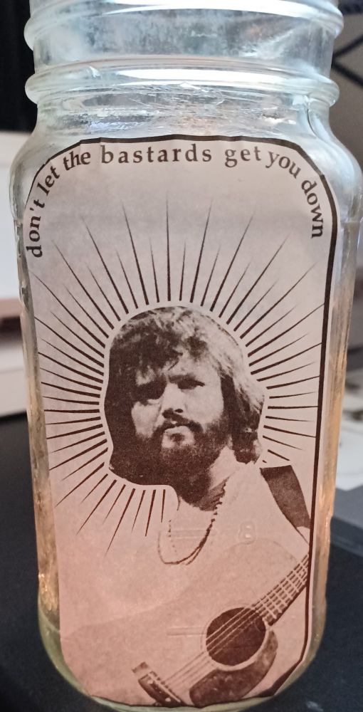kris kristofferson prayer candle rough prototype, photo of kris kristofferson with a guitar & a sort of halo with the text "don't let the bastards keep you down" above it
