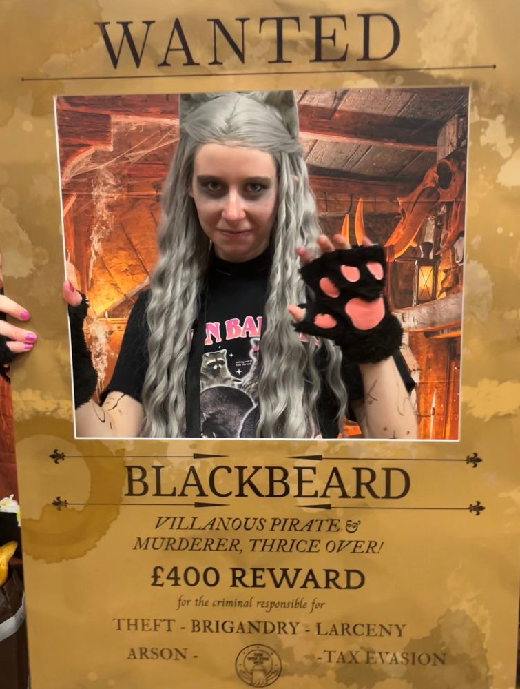 alice with kitty ears and grey wig with a black kitty paw held up behind a wanted poster reading:
Wanted
Blackbeard
Villainous pirate & murderer, thrice over!
£400 reward 
for the criminal responsible for
theft brigandry larceny arson tax evasion