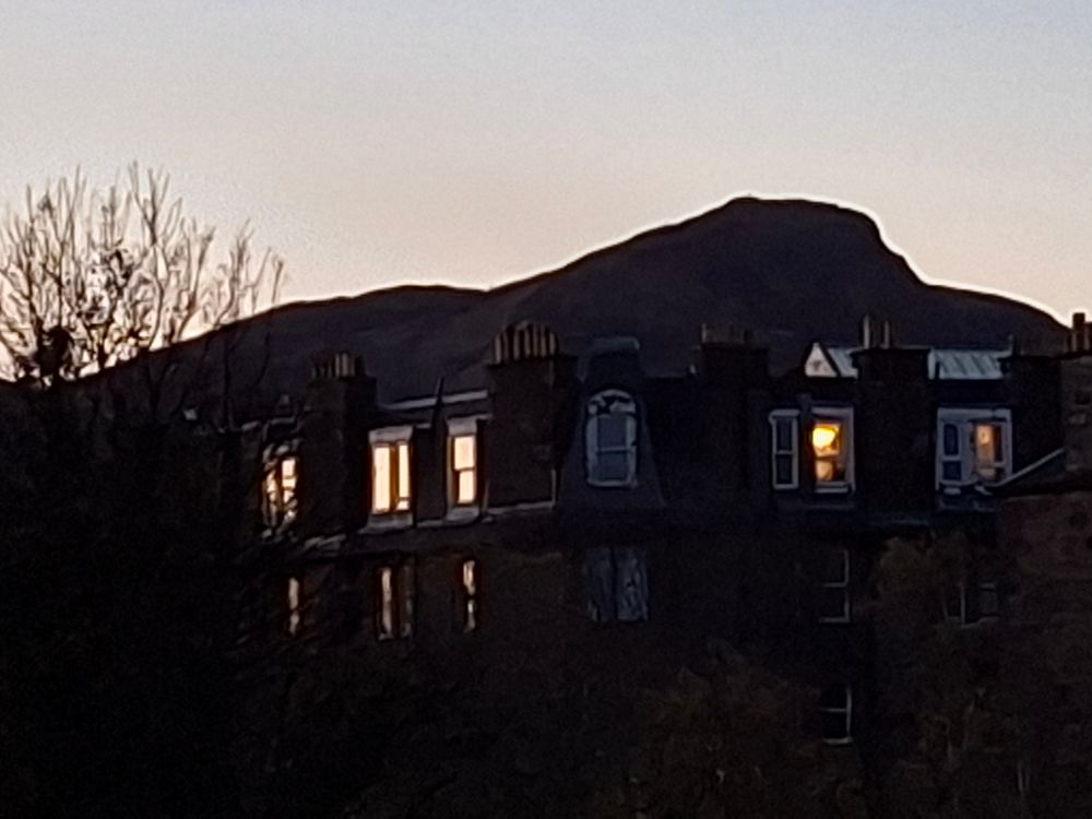 Flat windows of Leith reflecting the dim morning sun. Arthur's Seat is the background.
