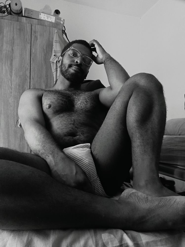A man, sitting on a chair, showing his legs, pecs and bulge. 