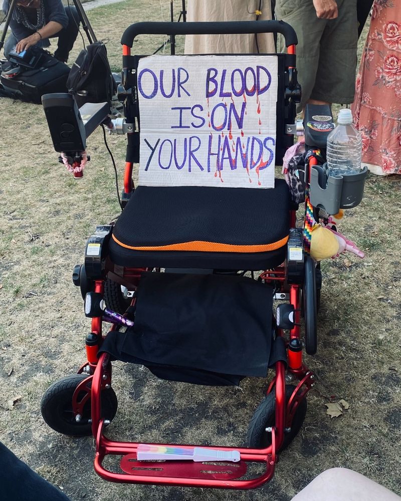 A wheelchair with a sign on it that says "our blood is on your hands"