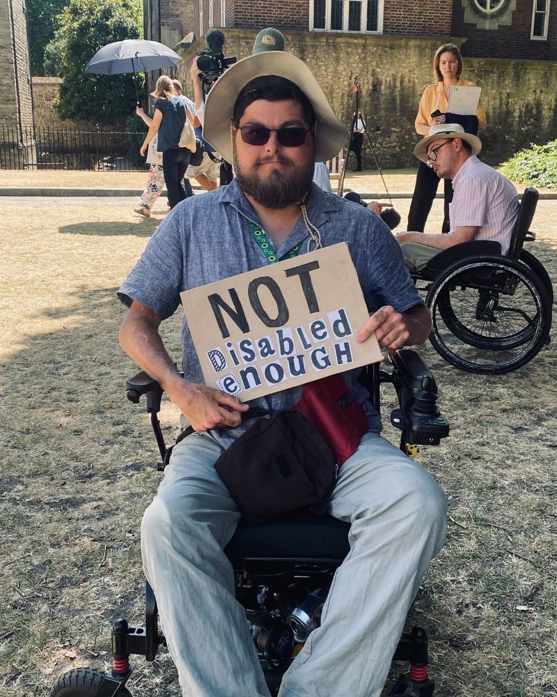 A person in a wheelchair with a sign that says "not disabled enough"