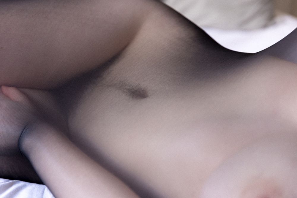 Soft focus shot of Margot in a black body stocking, from just under her breast to the top of her thighs. Her bush peeks through the fabric. 