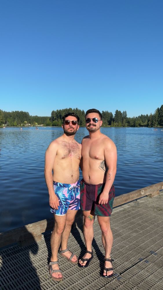 Two shirtless men in sunglasses standing on dock on lake