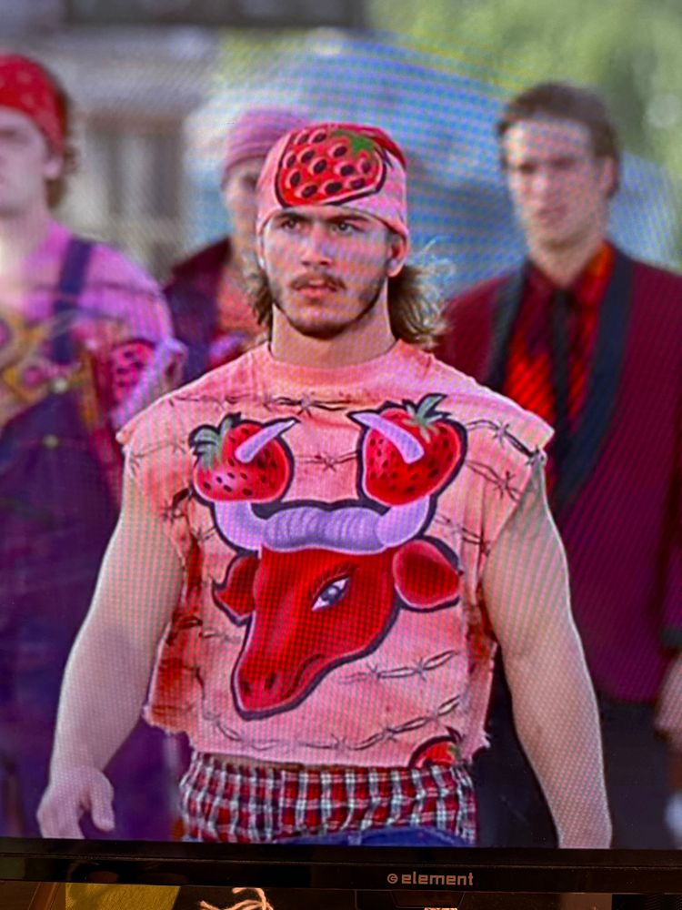 Screenshot of Too Wong Foo movie. Muscular man in bandana with strawberry print on it. Shirt with Red Bull with strawberries on horns. 