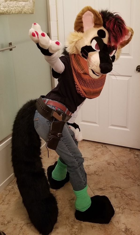 Bandit ferret fursuit but wearing the clothes of the Dragonball Z character Android 17. He has angry eyelids on. He is slightly facing away from the viewer, but is turned, looking at the viewer, with his right hand outstretched outward towards the viewer.