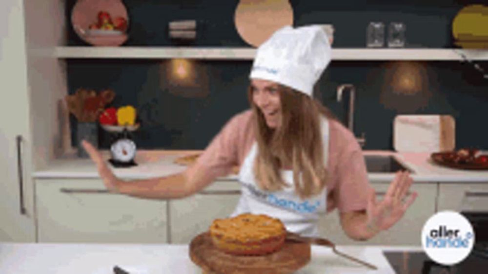 a woman in a chef 's hat and apron stands in a kitchen