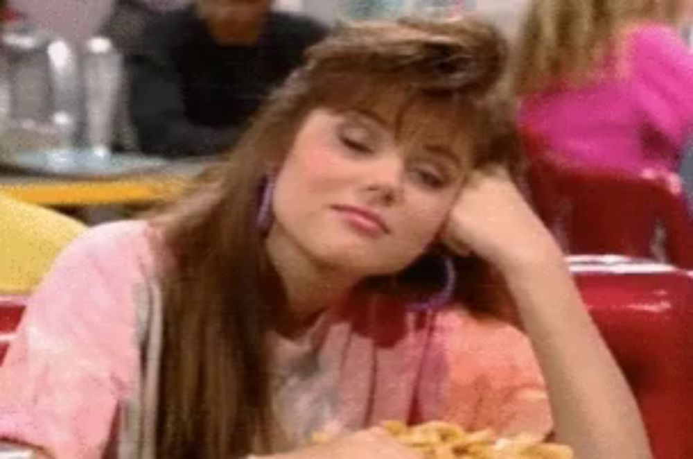 a woman in a pink shirt is sitting at a table with a plate of food .