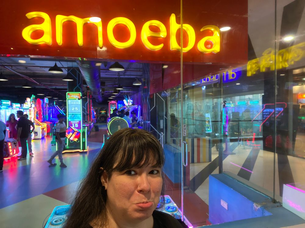 Jen looking sad in front of an arcade named amoeba 