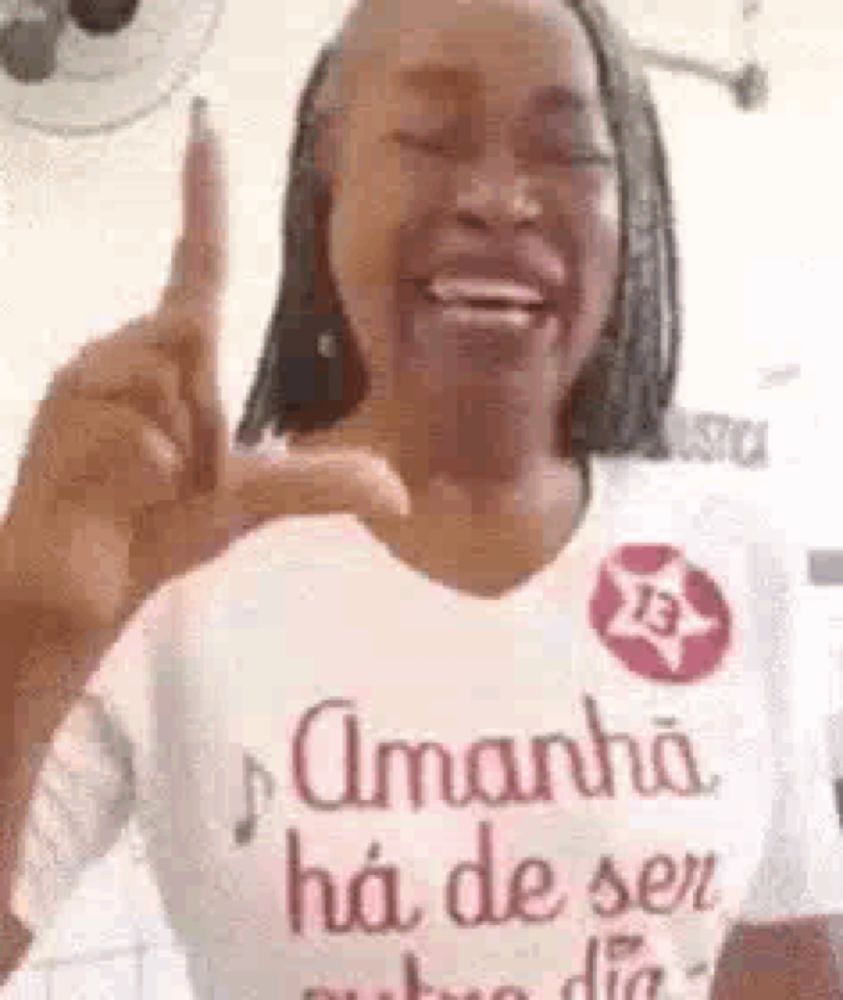 a woman wearing a t-shirt that says amanha ha de ser is giving a peace sign .