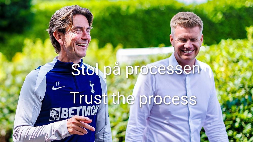 A photo of two men, Thomas Frank and Johan Lange walking around Tottenham Hotspur Training ground. Frank is on the left wearing a navy and white training top. Lange is on the right in a swagless white dress shirt. 

Text is overlaid on the image. The top text is Danish and says "Stol på processen". The bottom text is the English translation and says "Trust the process".