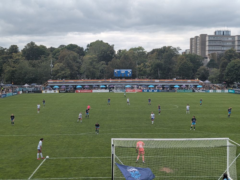 A photo of a football pitch in Halifax, Nova Scotia. It's the Wanderers Grounds and one team, wearing white, is taking a goal kick. The scoreboard shows a score of Tides 1 - Rapid 0