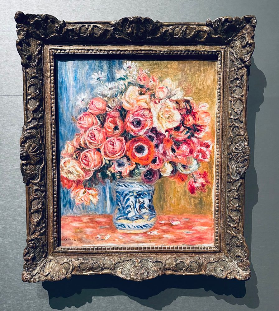 A painting with colourful roses and anemones in an artful frame. It is an Pierre-Auguste Renoir from 1910! 