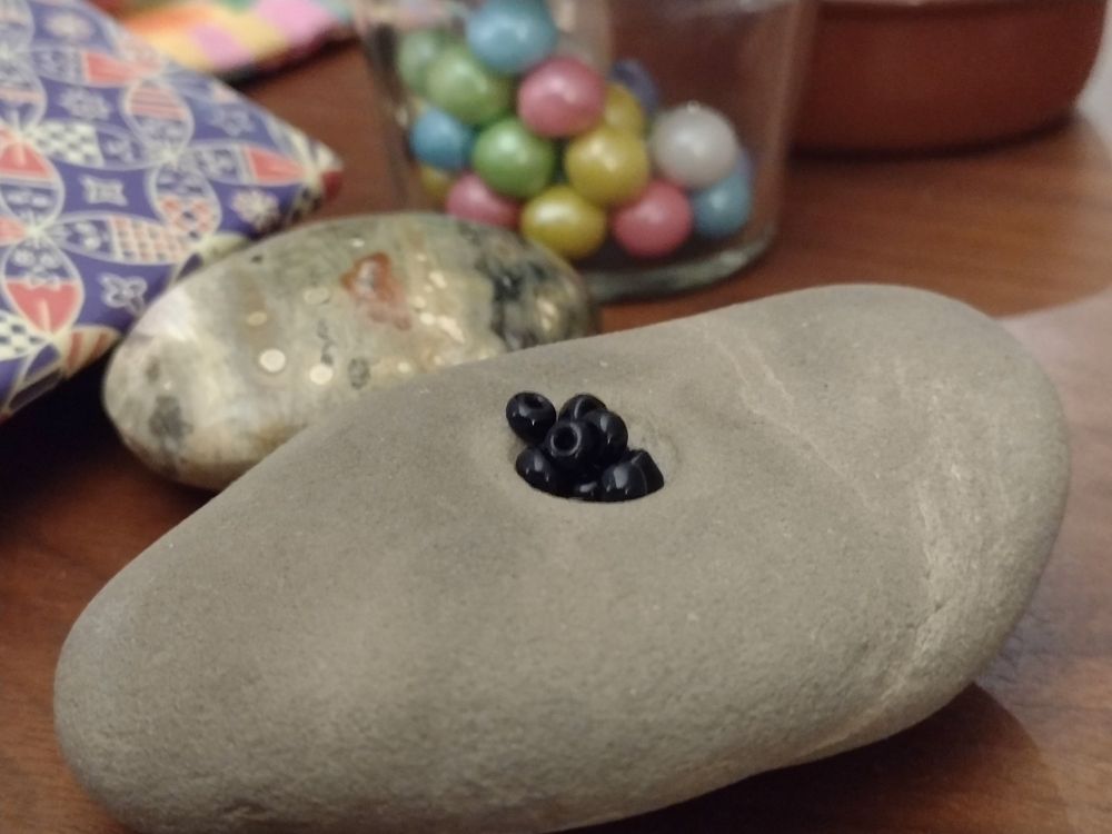 Close up of about ten small black beads nestled in a natural circular divot in a smooth gray stone