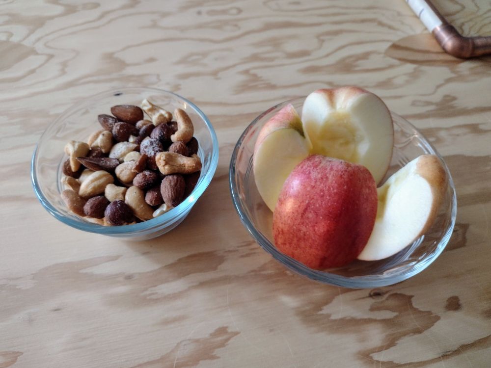 Two small glass bowls, one full of mixed nuts and one full of apple slices