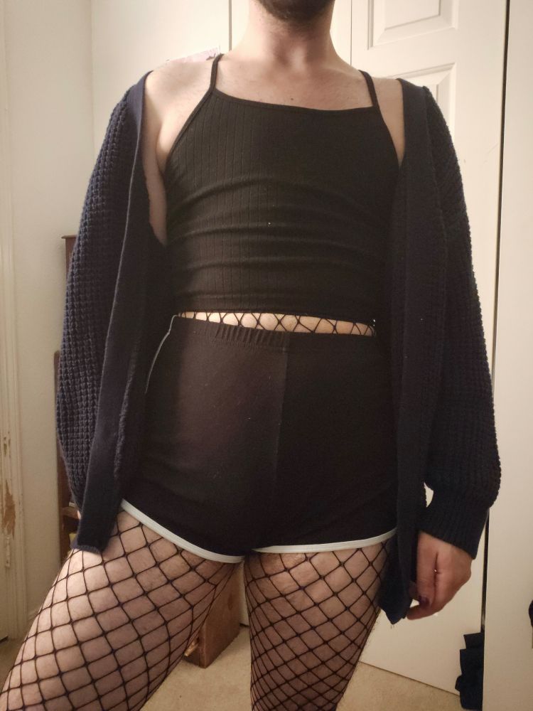 Rue in a navy cardigan hanging on his shoulders, black crop tank top, fish nets, and black booty shorts. 