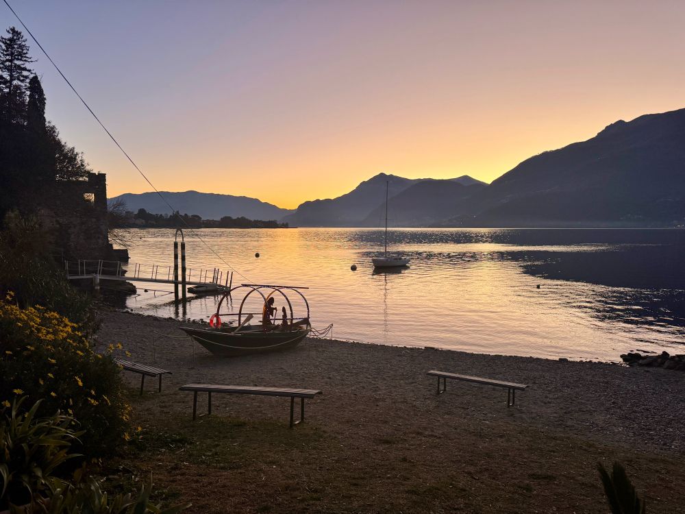 Corenno sunset, a boat on the sand and mountains in the distance across the lake