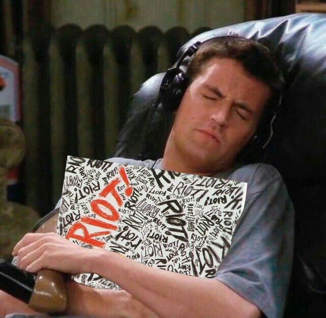 man holding riot! Record by paramore with headphones on sitting in a black leather chair closing his eyes