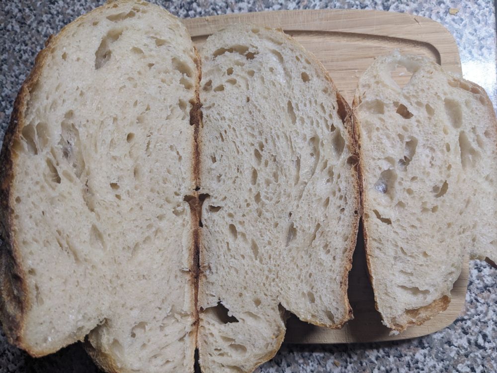 Top down view of a loaf of bread on a cutting board, showing the inside (crumb) of the loaf. Air holes are fairly eveningly distrubuted.