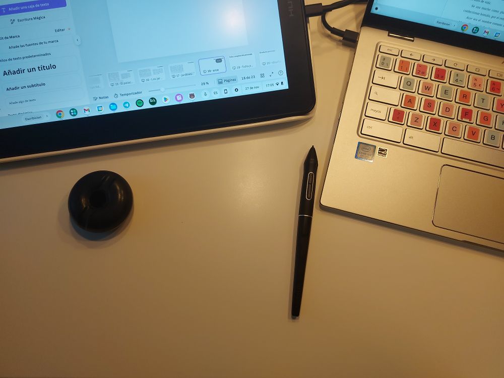 Foto de la mesa, donde se ve parte de la tableta gráfica, parte del portátil, el donut donde se deja el lápiz y el susodicho lápiz a un palmo del donut, encima de la mesa.