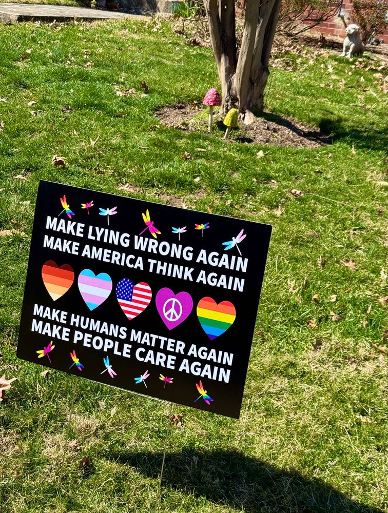 A yard sign promoting peace and equality in a grassy yard