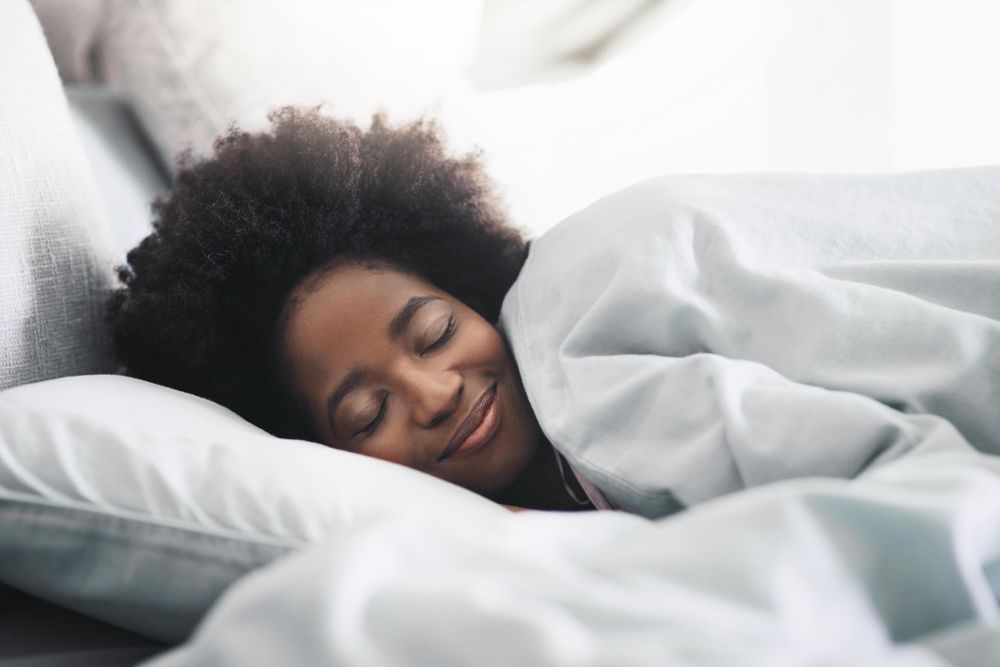 A woman is sleeping in a bed with white bedding. Covers are pulled up to her neck.