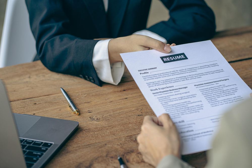 two professionals hold resume at desk with laptop 