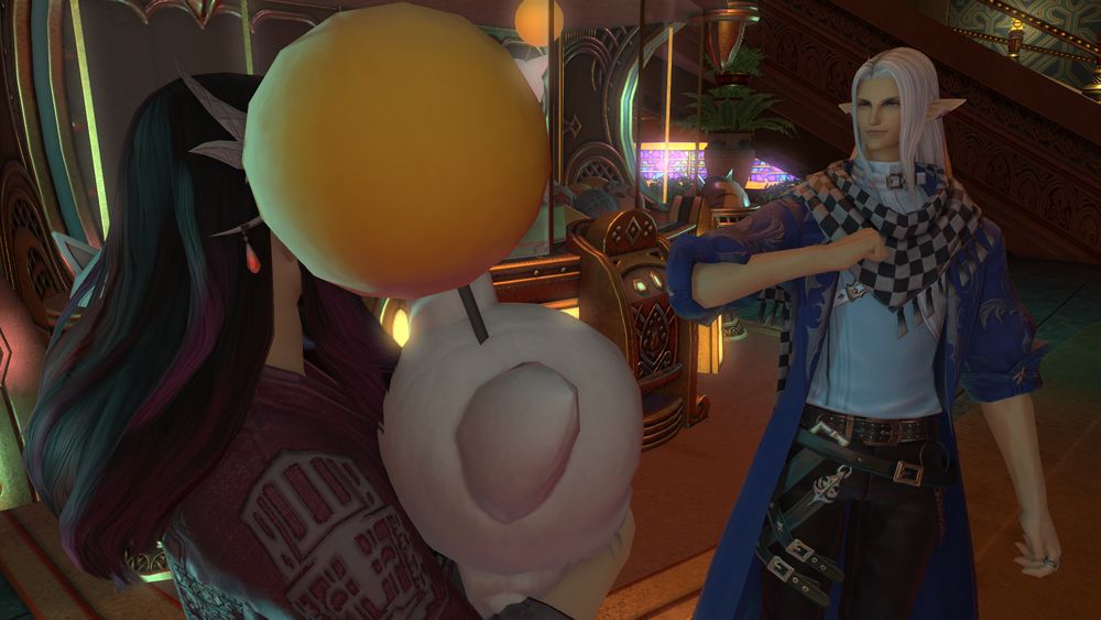 Lia e Erdan parados em frente a uma máquina de bichinhos na Gold Saucer. Lia está abraçada com um moogle de pelúcia, enquanto Erdan aponta para si mesmo com um sorriso triunfante no rosto