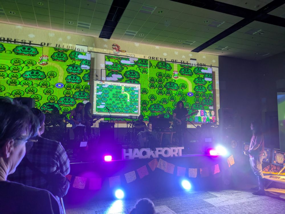Bit Brigade performing Super Mario World at Hackfort. A band playing the SMW soundtrack live while a player speedruns through the game, as displayed on large screens.