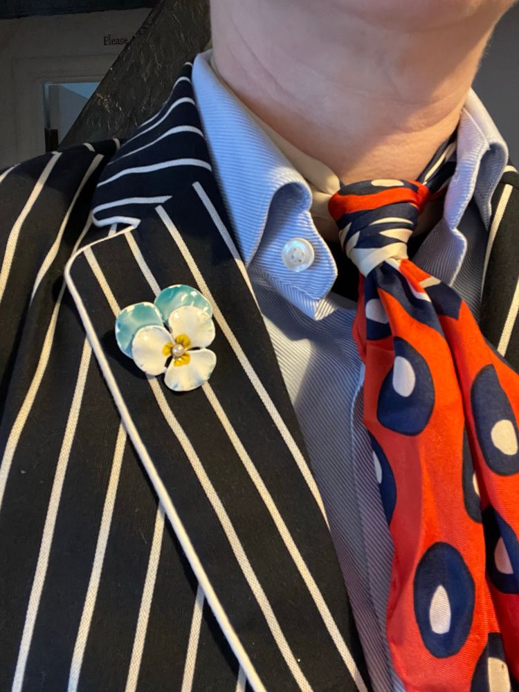 We know it’s about the details. A light blue and white pansy pin with a pearl center on a navy and white pinstripe blazer.
