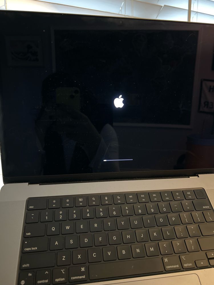 Day’s MacBook installing an update, showing a black screen with the apple logo and a tiny sliver of the progress bar at the bottom.