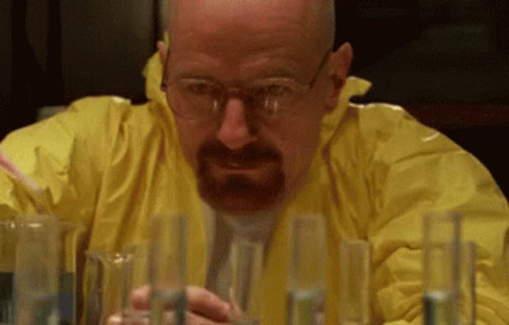 a man with a beard is wearing a yellow jacket and glasses while looking at beakers .