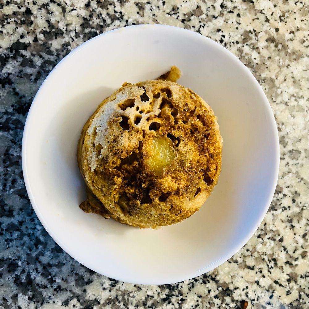 An individual serving apple dumpling cake sitting on a plate, plate is on a counter