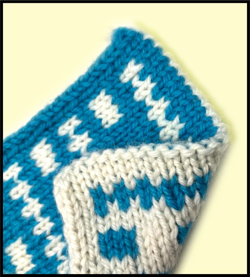 A purl graft at the top of a blue and white double knitting project. The graft makes a fold line, applying a contrasting color line of purls to one side, and a line of attractive bumps in same color, to the other. 