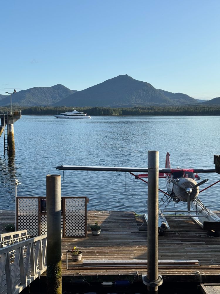 Float plane parked on a dock in the foreground. Sea and mountains behind.