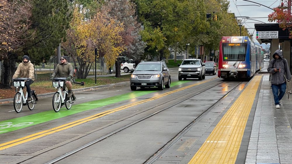 Bike share riders, cars, and light rail on a rainy street in Salt Lake City. Photo by Greg Griffin