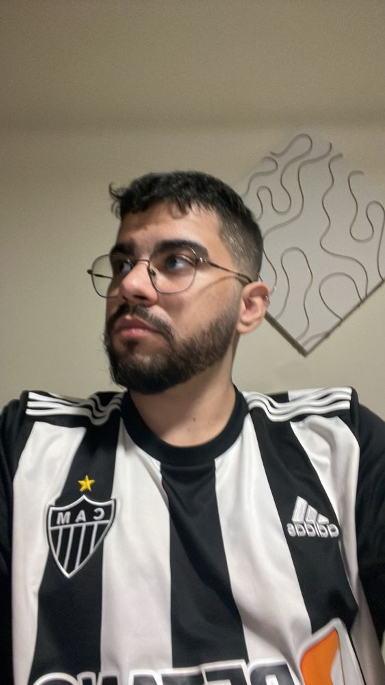 uma selfie minha com camisa listrada preta e branca do galo olhando pro lado

tenho cabelo e barba pretas, uso óculos com armaçao arredondadas