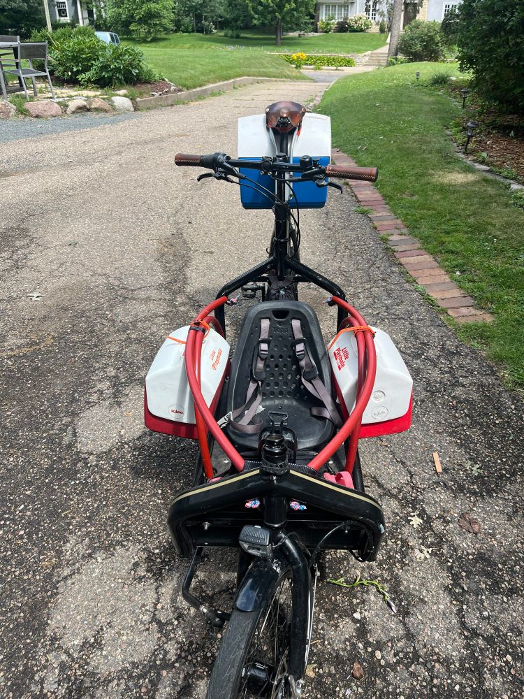 A Bullitt bike with 3 coolers strapped to it, two red and one blue behind the saddle.