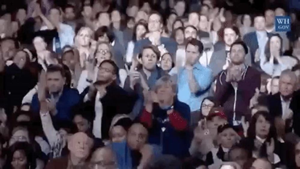 a large group of people are sitting in a stadium applauding and clapping .